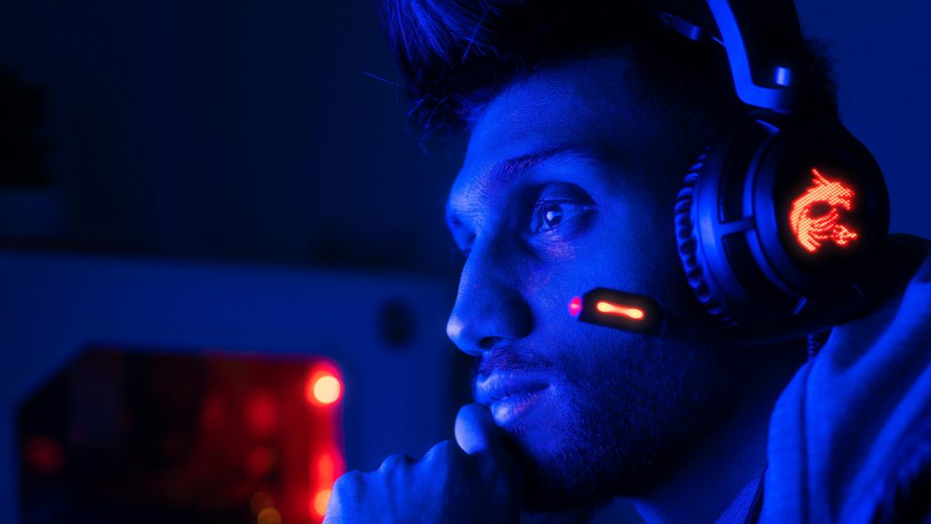 Close-up of a focused gamer with headset in blue lighting, embodying intense concentration.